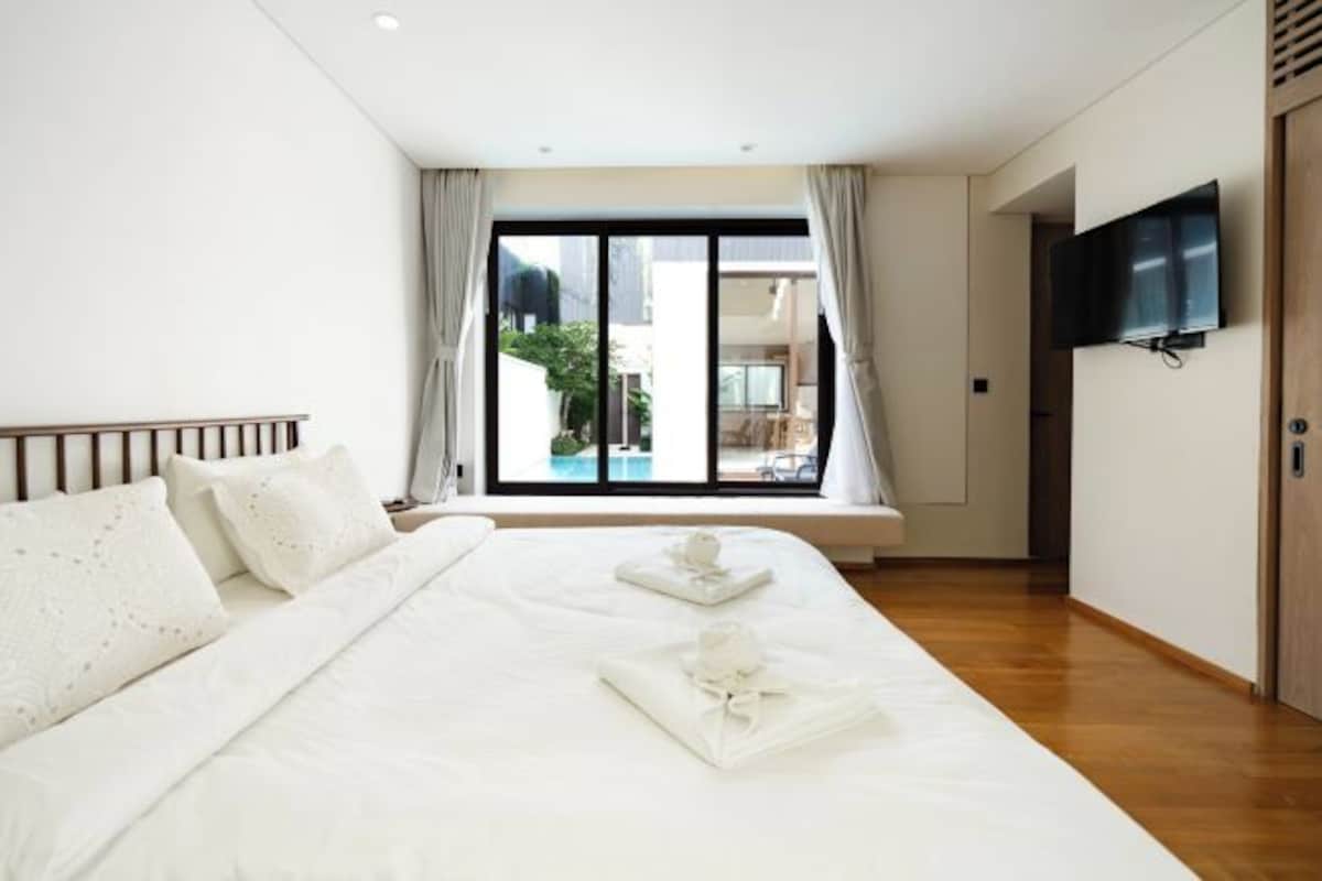 Habitación de hotel con una cama grande, un televisor montado en la pared y vistas a una piscina por la ventana.
