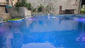 A swimming pool with a tiled edge, surrounded by plants and a concrete wall. - Dok Champa Hotel (Vang Vieng)