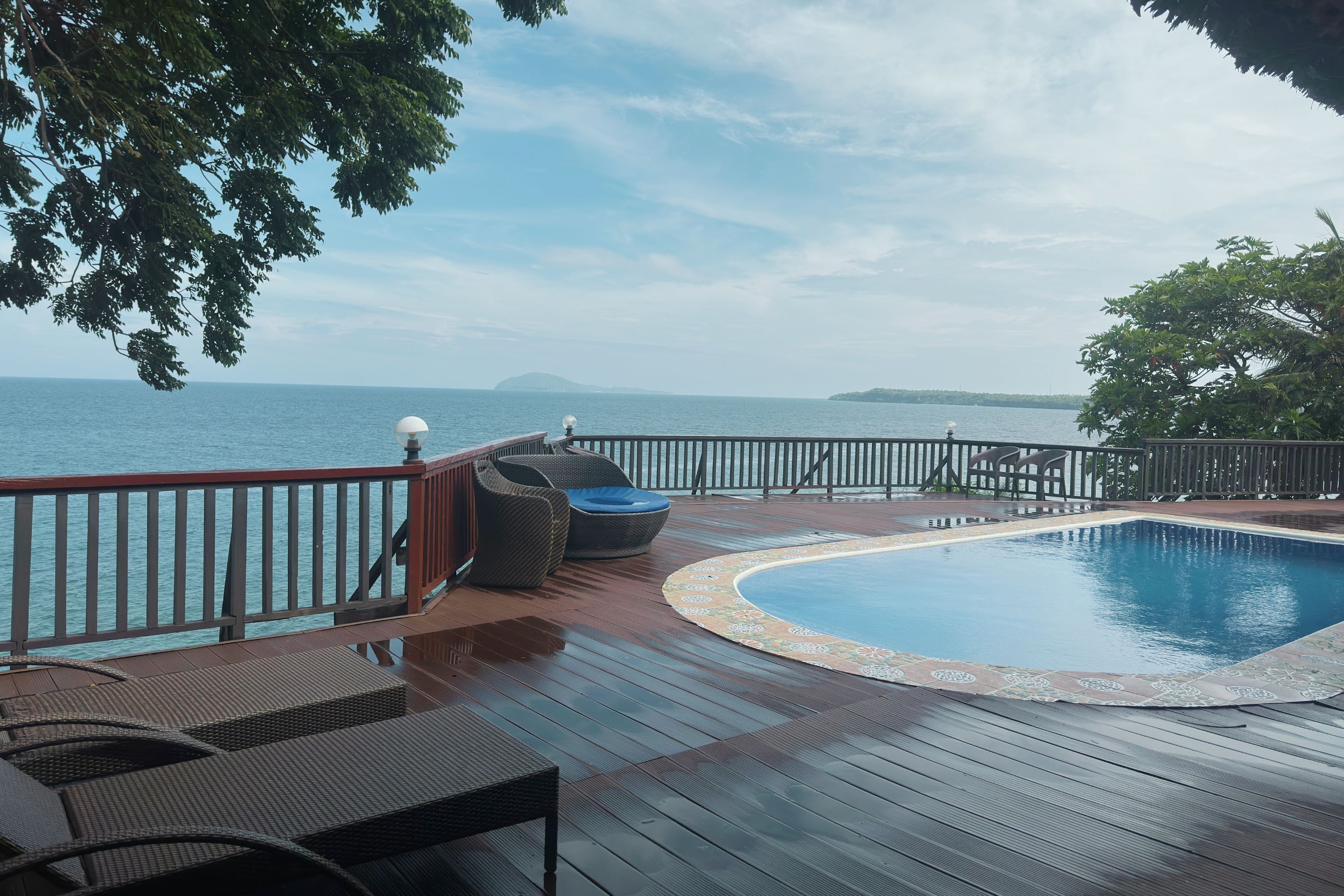 A wooden deck with a pool, lounge chairs, and a view of the sea.