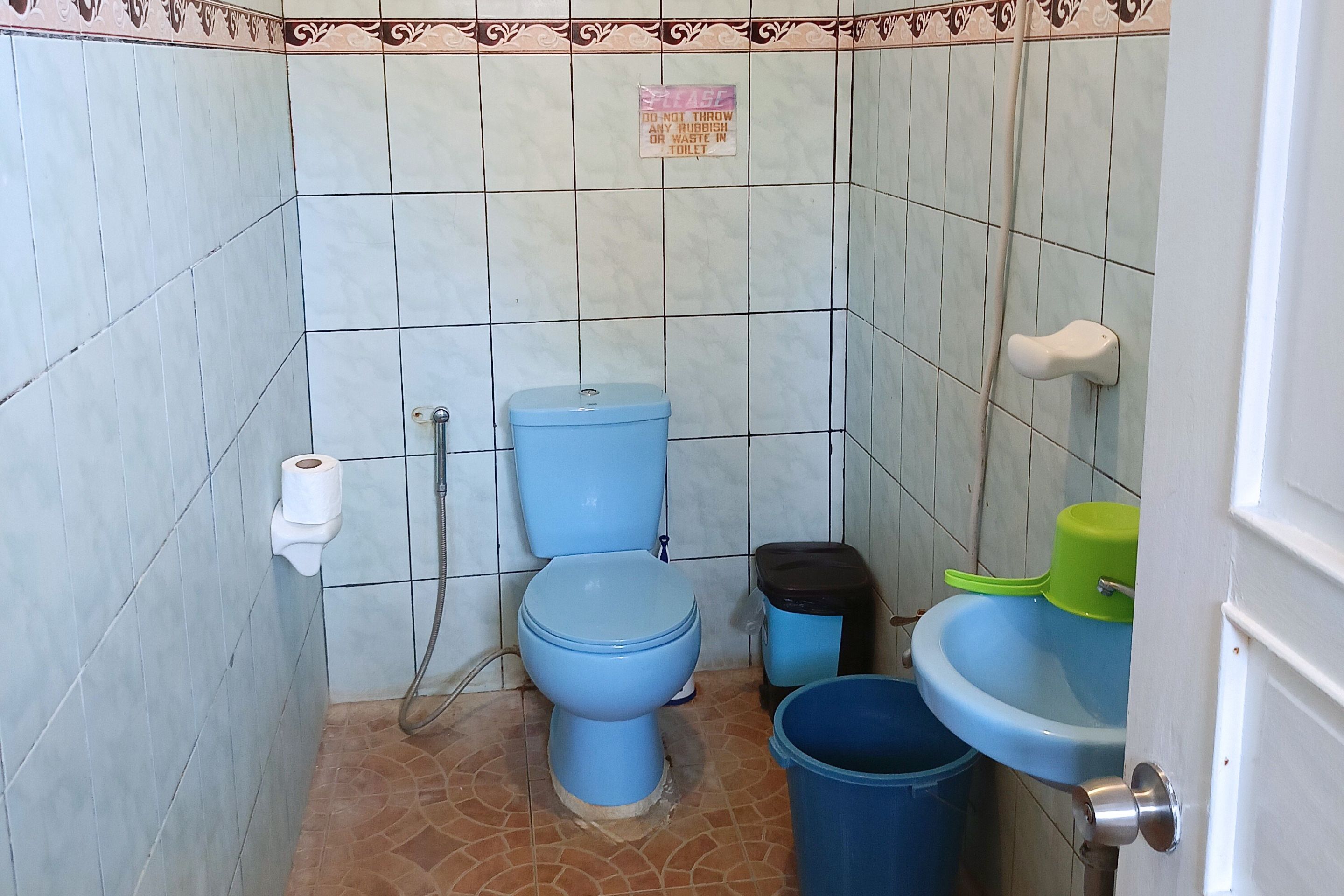 A small bathroom with a toilet, bidet, and sink. There is a trash bin and a toilet paper holder.