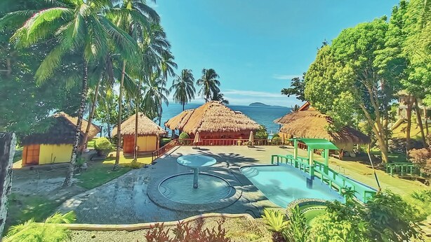 A resort with thatched-roof huts, a swimming pool, and palm trees. - Blue Deep Resort powered by Cocotel (Padre Burgos)