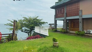 A two-story building with a balcony overlooking a body of water, surrounded by greenery and a wooden fence. - Blue Deep Resort powered by Cocotel (Padre Burgos)