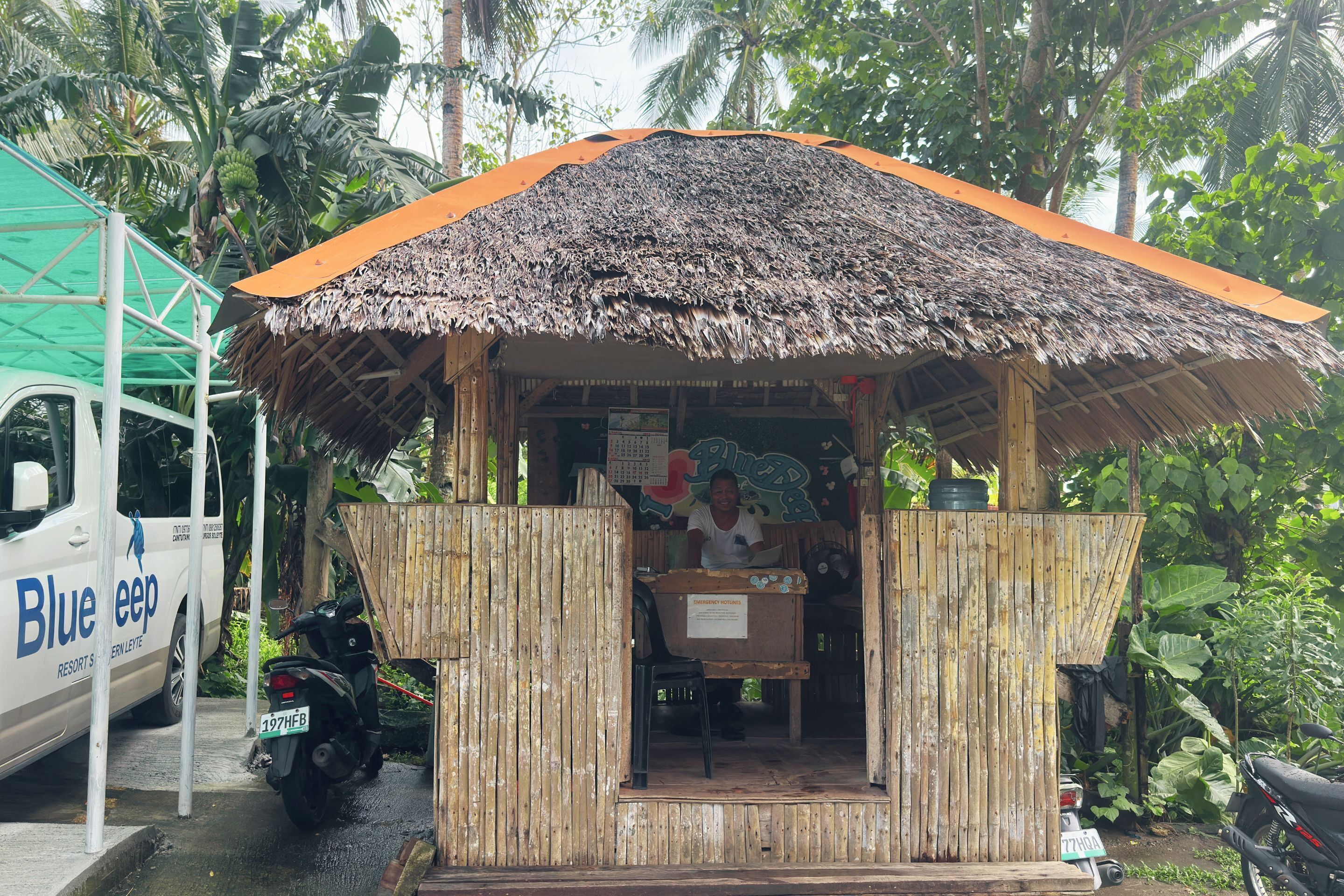 A small wooden structure with a thatched roof, a signboard, and a motorcycle parked nearby.