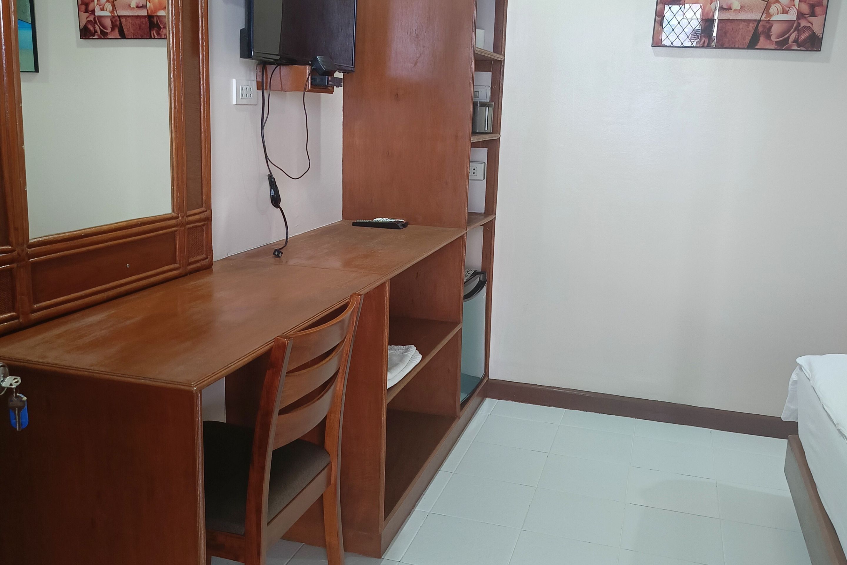 A wooden desk with a chair, a television mounted on the wall, and a bookshelf.