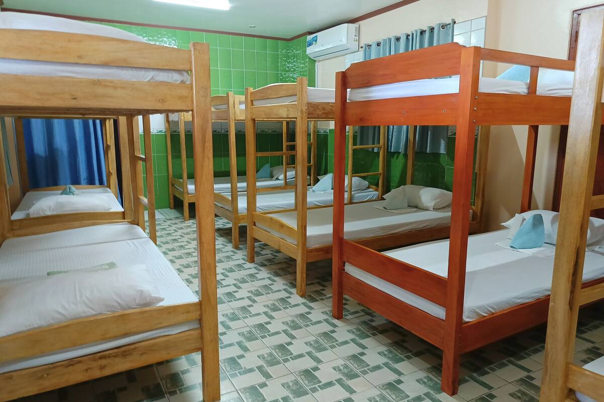 Une chambre avec des lits superposés, des murs recouverts de carreaux verts et un appareil de climatisation.