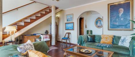A spacious living room with a staircase, a green sofa set, a wooden coffee table, and a chandelier.