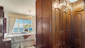 A bedroom with a large wooden wardrobe, a bed with a view of the sea, and a chandelier. - Villa Bom Sucesso (Funchal)