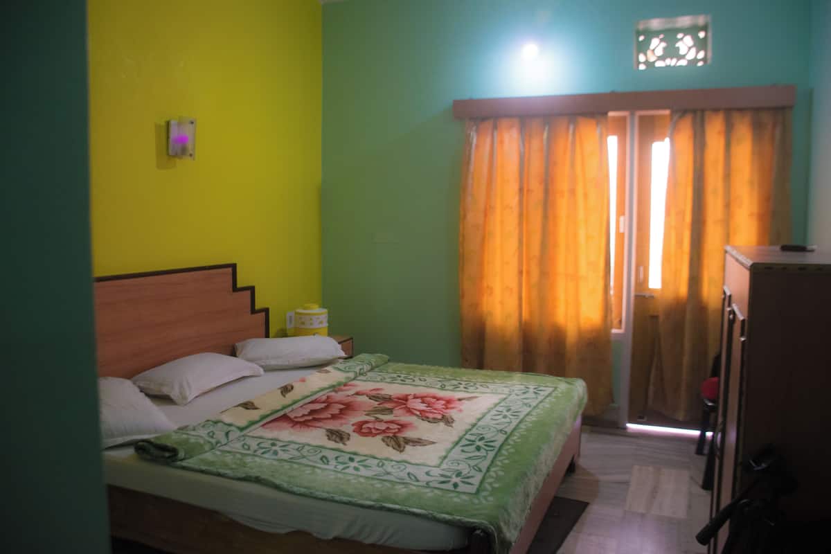A room with a bed, a nightstand, a lamp, and a window with curtains.