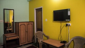 Quarto com guarda-roupa de madeira, espelho, televisão na parede e duas cadeiras de vime.