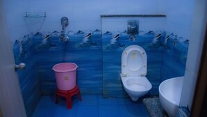 Um banheiro com parede azulejada em azul, vaso sanitário branco, um balde rosa e pia branca.