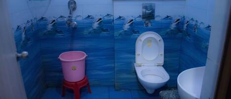 A bathroom with a blue tiled wall, a white toilet, a pink bucket, and a white sink.
