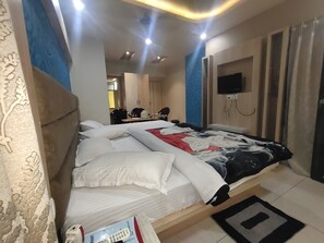 A hotel room with a bed, a TV mounted on the wall, and a desk with chairs. - Hotel Suv Palace (Puri)