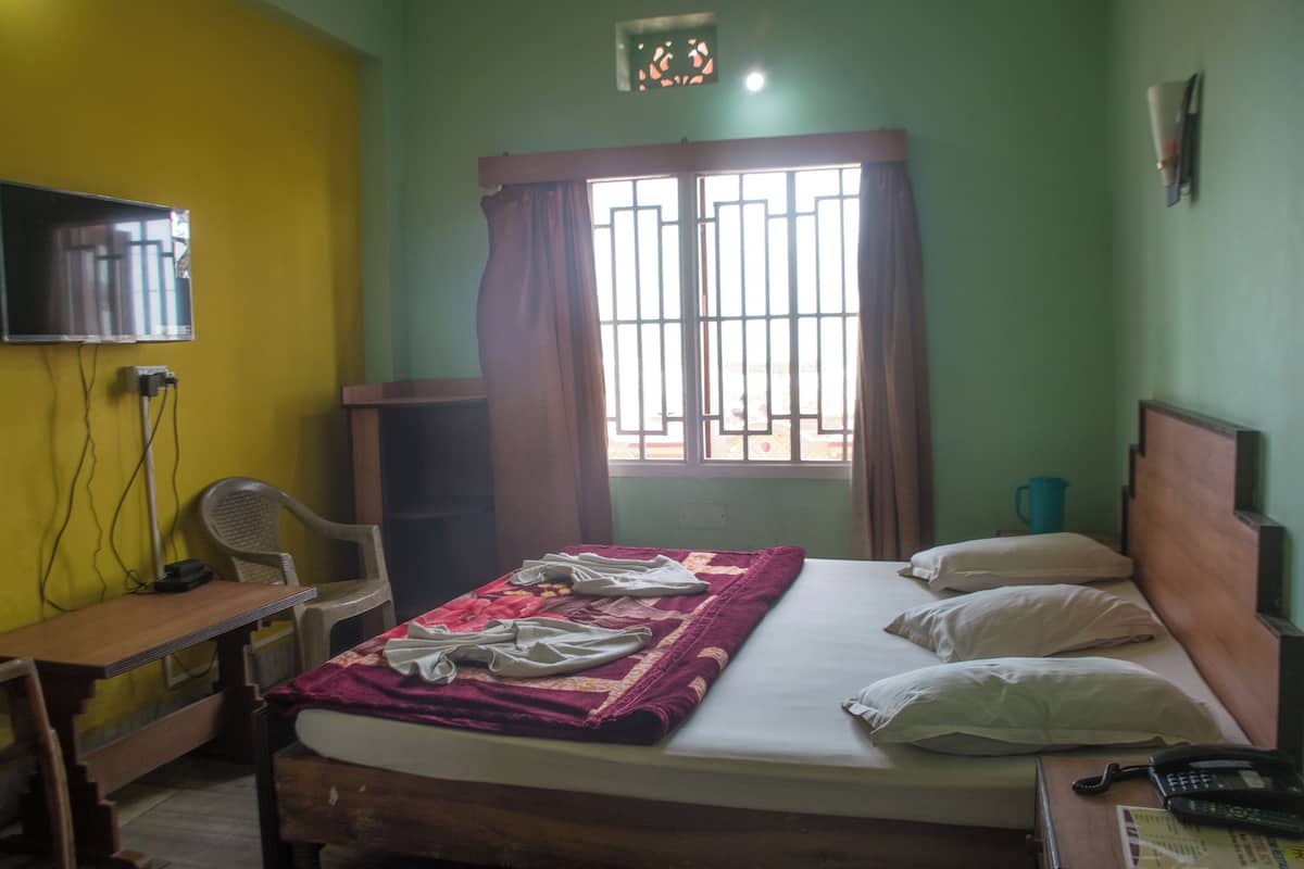 A bedroom with a bed, a desk, a chair, a TV, and a window with curtains.