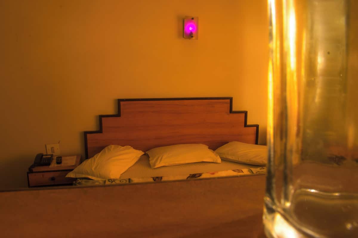 A bed with a wooden headboard, a nightstand with a phone, and a wall-mounted light.