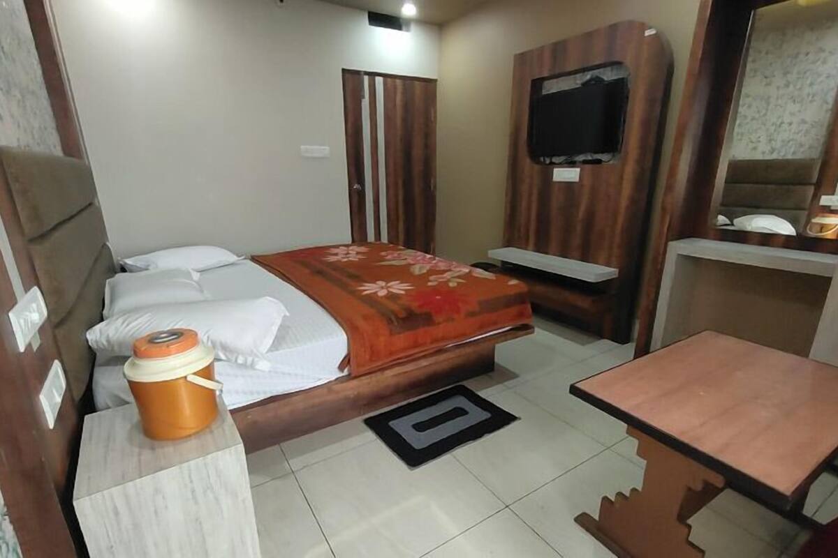 A compact hotel room with a bed, a small table, a television mounted on the wall, and a wooden wardrobe.
