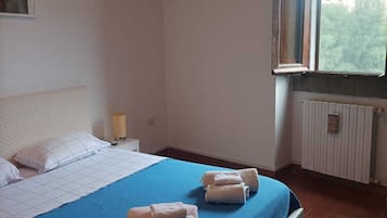 Ein Schlafzimmer mit einem Bett, Kissen, einem Nachttisch, einer Lampe und einem Fenster mit Vorhängen.