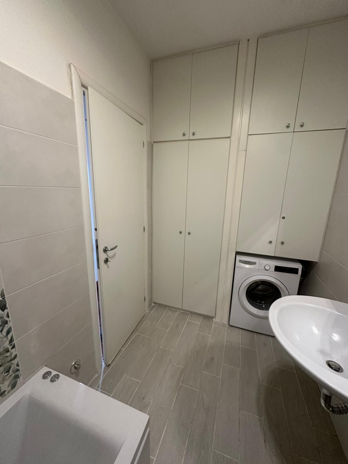 A bathroom with a bathtub, a sink, a washing machine, and tiled walls.