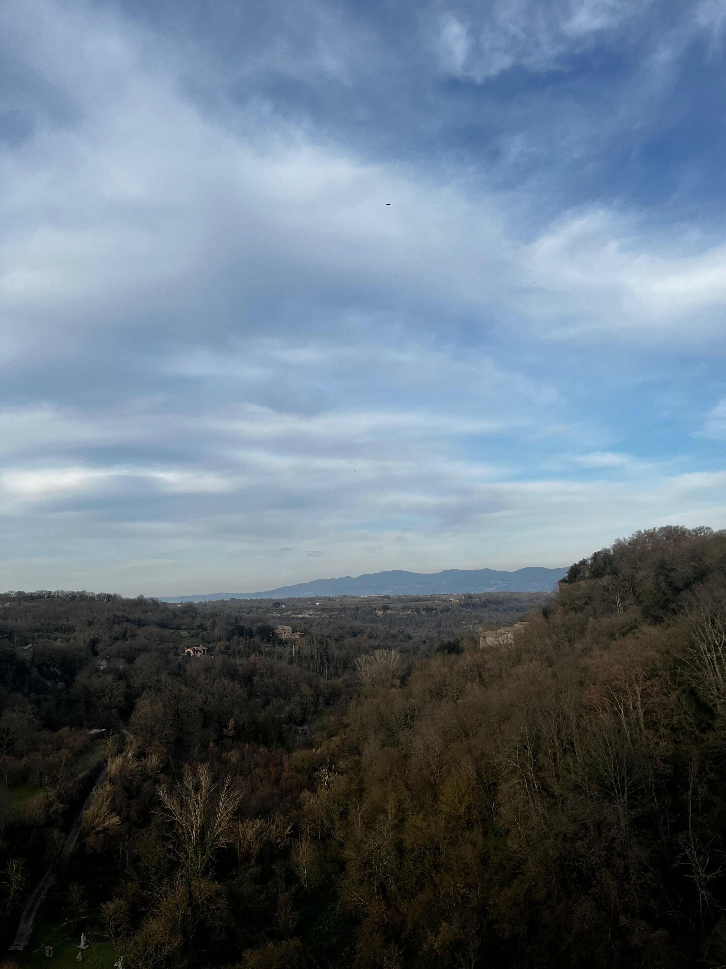 A panoramic view of a hilly landscape with scattered buildings, a clear sky, and a distant airplane.