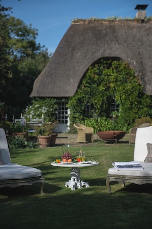 An outdoor seating area with a thatched-roof structure, a white dog statue, and a table with a fruit arrangement. - Le Domaine d'Ablon (Ablon)