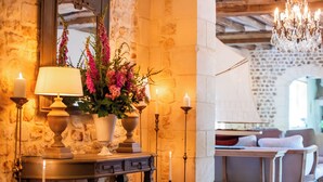 A cozy room with a stone wall, a wooden table with a vase of flowers, and a chandelier. - Le Domaine d'Ablon (Ablon)