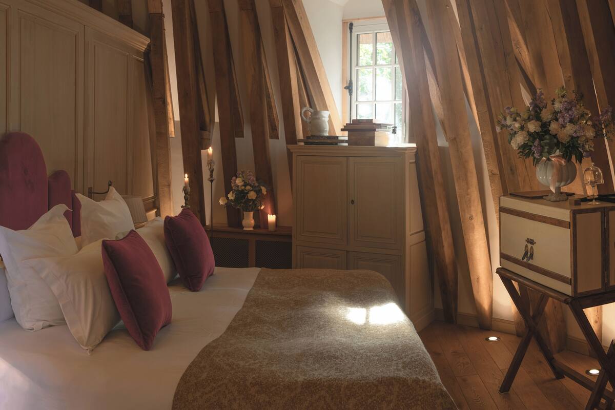 Ein Schlafzimmer mit schrägverdeckter Decke, einem Bett mit weißer und roter Bettwäsche, einem Schminktisch und einem Spiegel.