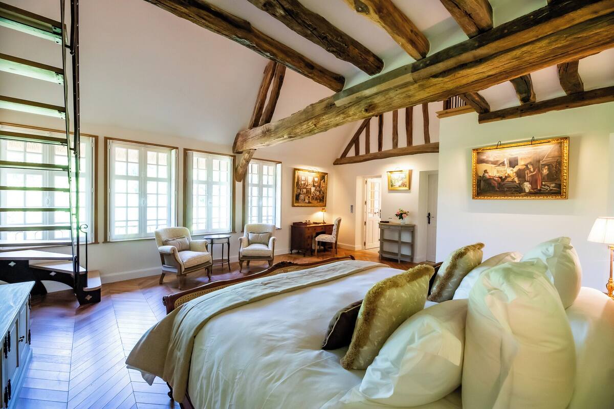 Ein Schlafzimmer mit einem großen Bett, Holzbalken, einem Schreibtisch und zwei Stühlen.