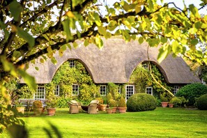 A thatched-roof cottage with ivy-covered walls, a well-maintained lawn, and outdoor seating. - Le Domaine d'Ablon (Ablon)