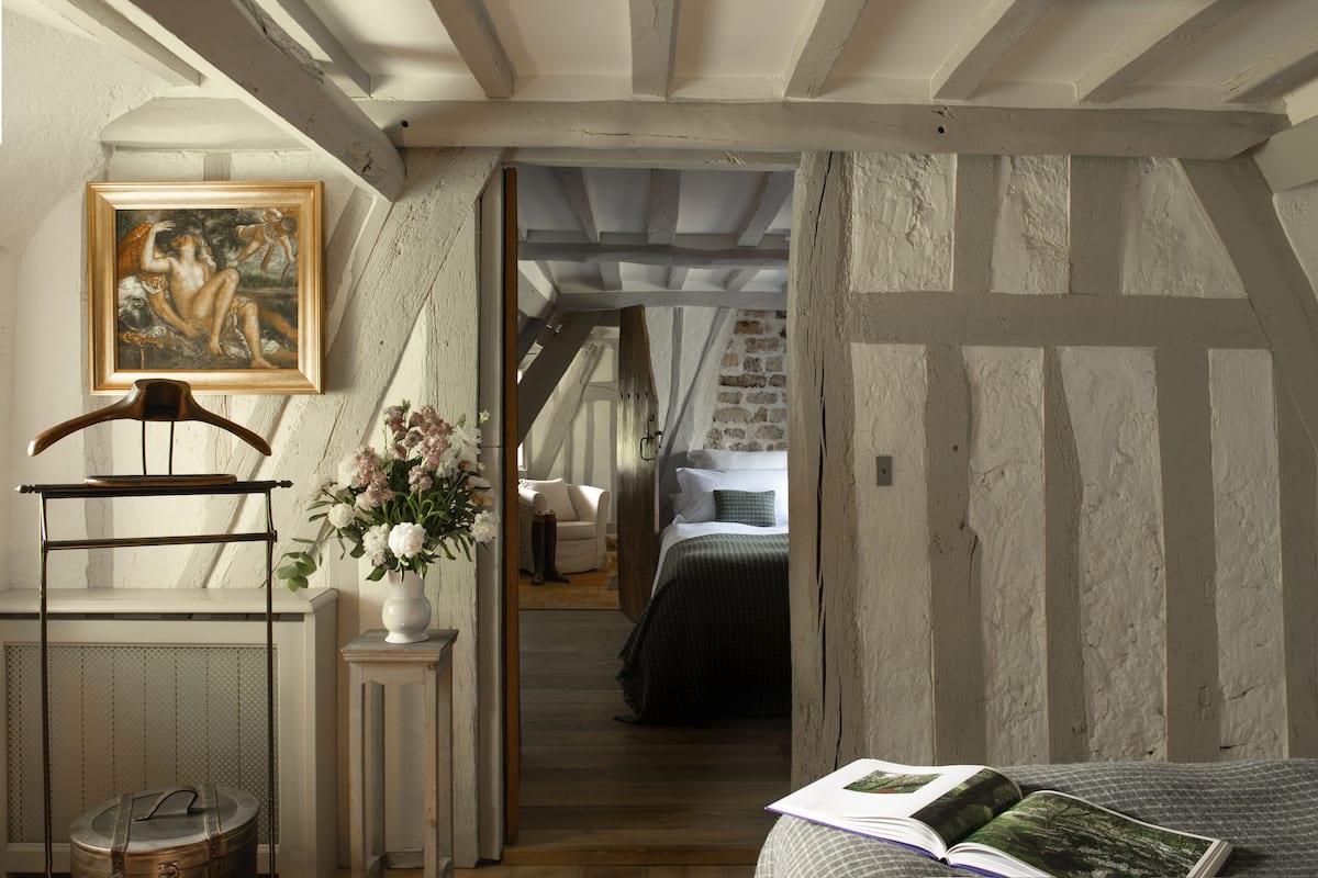 Ein gemütliches Schlafzimmer im Dachgeschoss mit freiliegenden Holzbalken, einer rustikalen Ziegelwand, einem hölzernen Bett und einem Gemälde an der Wand.