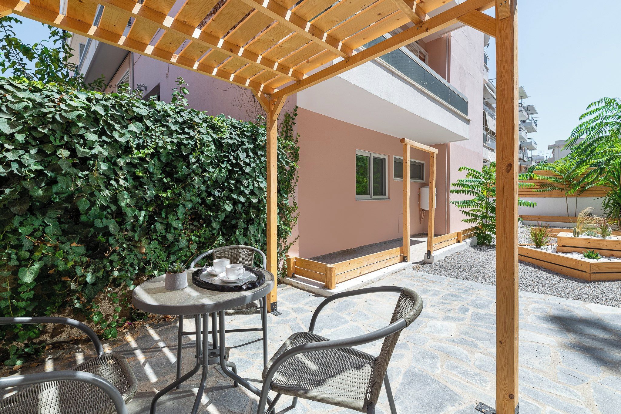 An outdoor patio with a wooden pergola, a round table with chairs, and a potted plant.