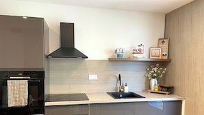 A modern kitchen with a built-in oven, a black range hood, a stainless steel sink, and a wooden countertop. - Charming 4-bedroom house with garden, close to shops and bus stop (Bruz)