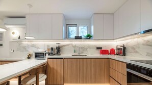A modern kitchen with a marble countertop, wooden cabinets, and stainless steel appliances. - Glyfada Coastside Apartment (Glyfada)