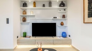A modern living room with a flat-screen TV centered on a white wall, surrounded by shelves with decorative items. - Glyfada Coastside Apartment (Glyfada)