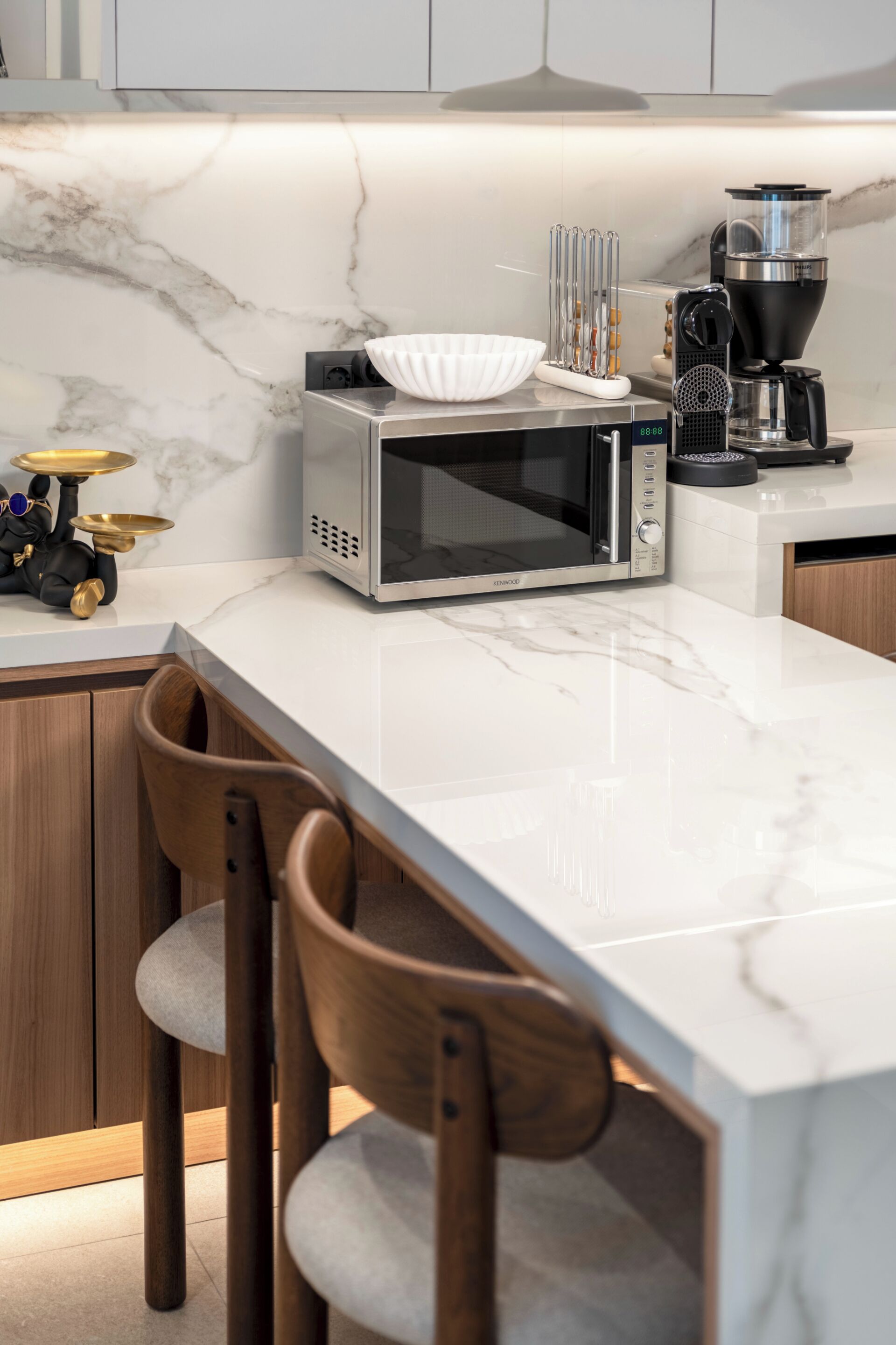 A kitchen with a microwave, coffee maker, and a marble countertop.