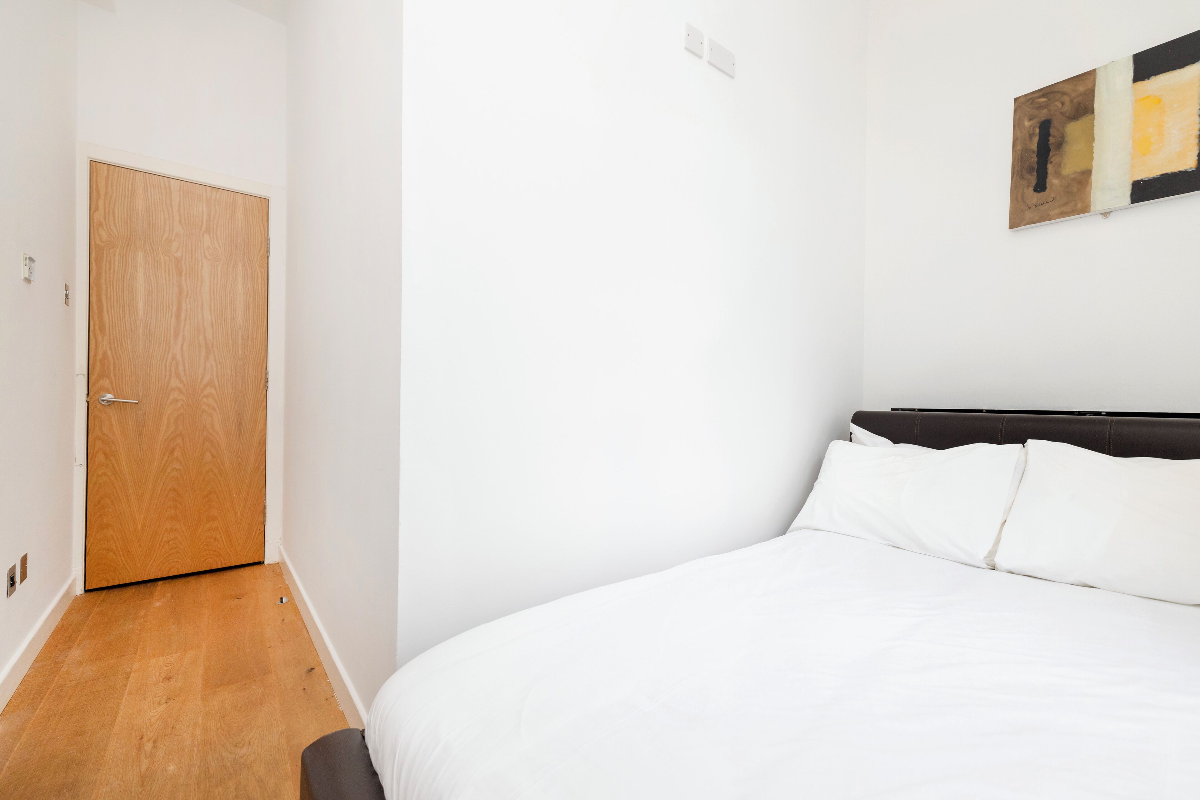 Ein Schlafzimmer mit Holztür, einem Bett mit weißer Bettwäsche und einem an der Wand hängenden Kunstwerk.