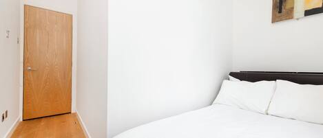 Ein Schlafzimmer mit Holztür, einem Bett mit weißer Bettwäsche und einem an der Wand hängenden Kunstwerk.