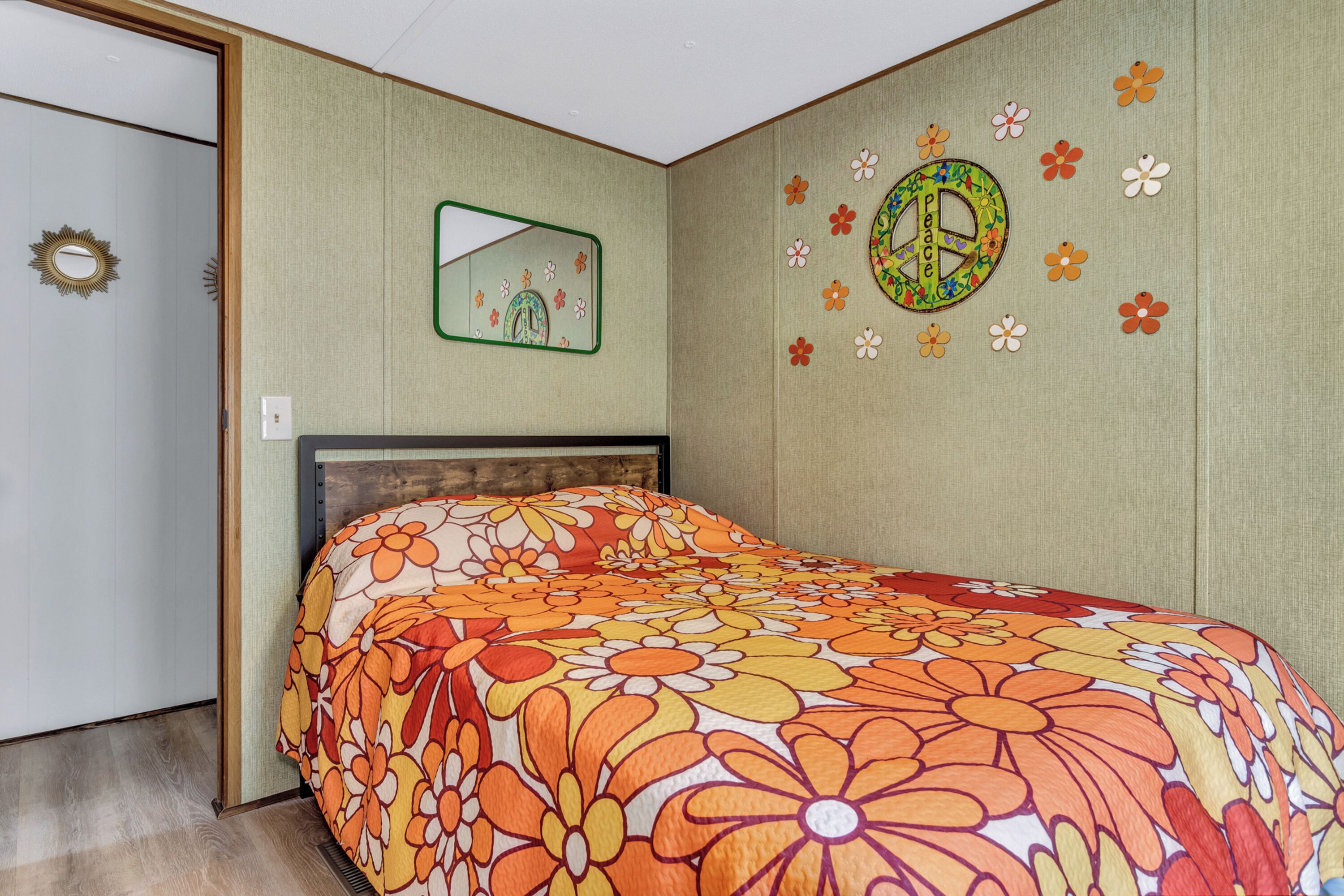 A bedroom with a floral bedspread, a mirror, and a wall with a peace symbol and flowers.