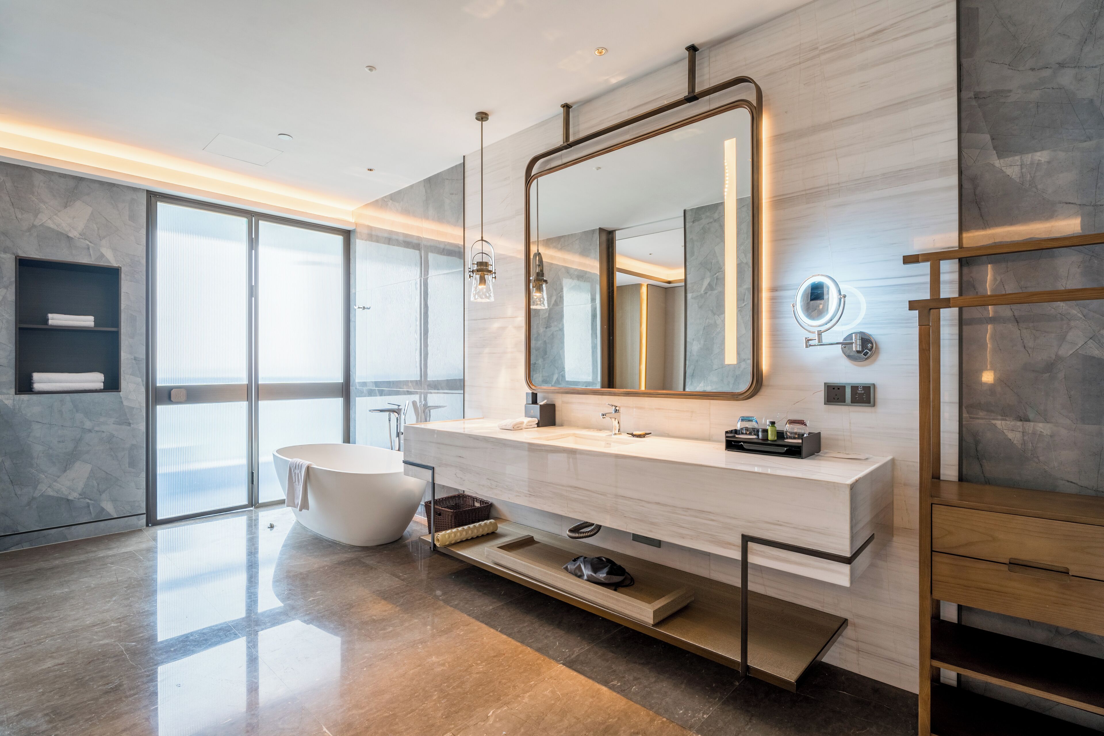 A modern bathroom with a large mirror, a freestanding bathtub, and a vanity with a marble countertop.
