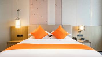 A hotel room with a bed, two orange pillows, a bedside lamp, a nightstand with a phone and a radio, and a wall with a floral pattern.