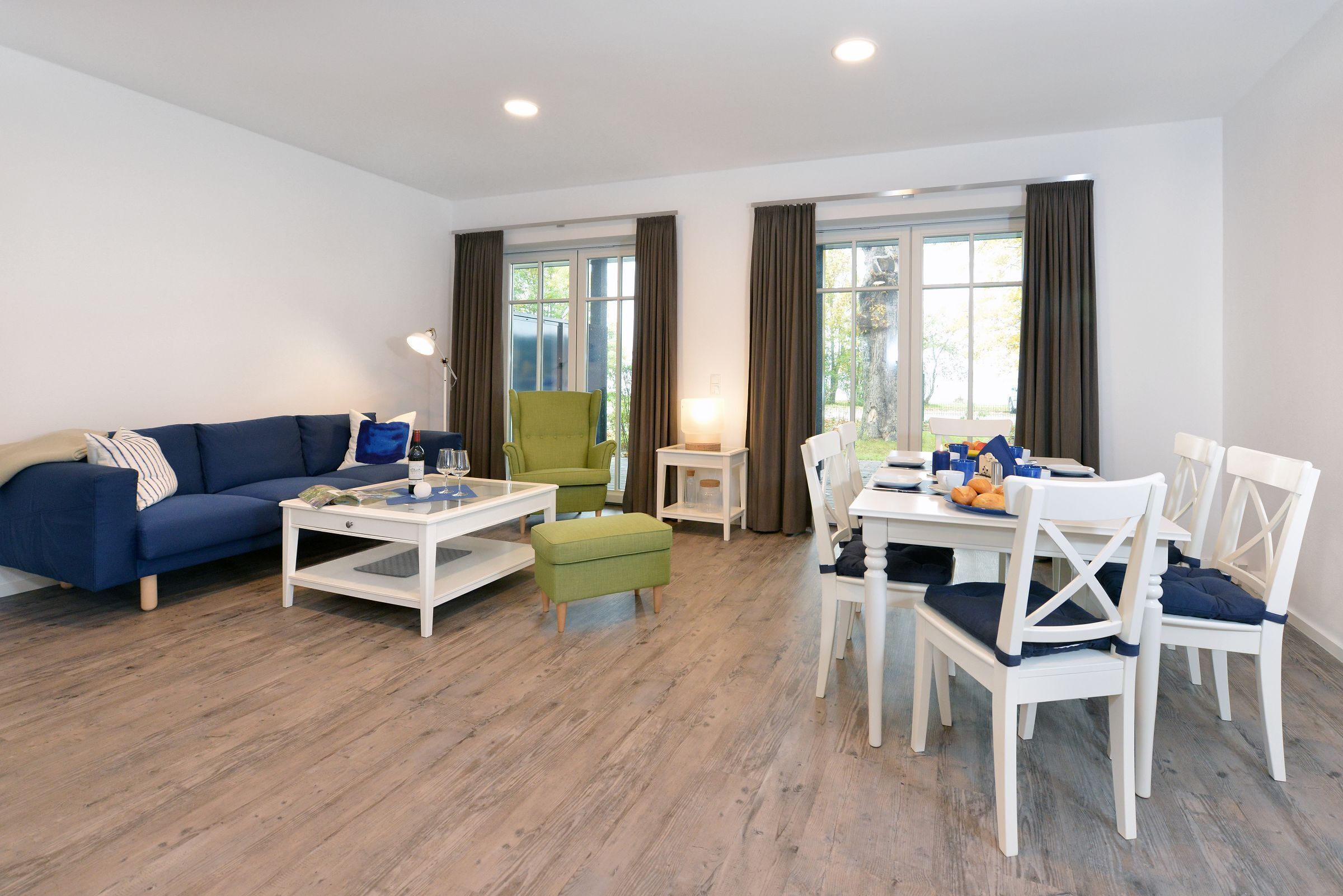 A modern living room with a blue sofa, a green armchair, a white dining table with chairs, and a small white side table.