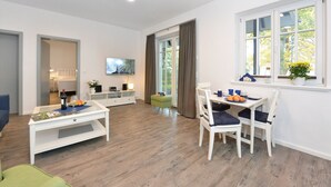 A spacious living area with a dining table, chairs, a sofa, and a television. - Comfortable vacation apartment with sea view and terrace in the Blue House in Ralswiek (Ralswiek)