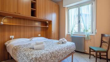Un dormitorio con cama, una silla, una ventana con cortinas y armarios de madera.