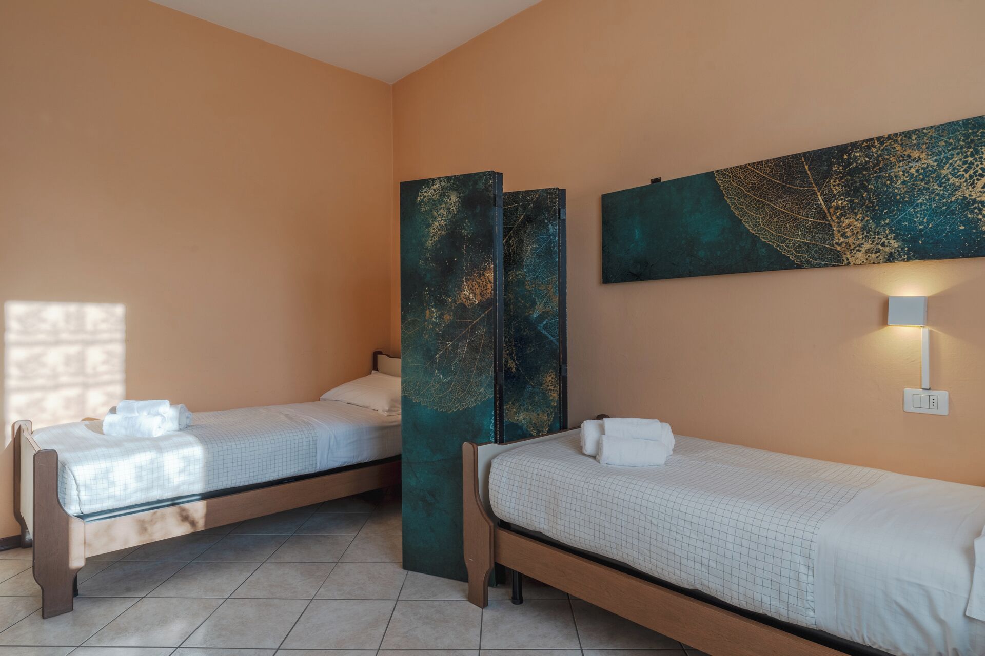Een hotelkamer met twee eenpersoonsbedden, een groot abstract schilderij aan de muur en een wandlamp.