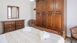 Quarto com um guarda-roupa de madeira grande, cômoda, cadeira e cama com toalhas dobradas.