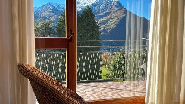 Un balcón con una silla de mimbre, vista a montañas nevadas y cielo despejado.