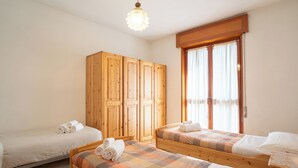 Una habitación con dos camas de madera, un armario y una ventana con cortinas.