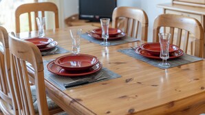 Una mesa de comedor con platos rojos, vasos transparentes y sillas de madera.