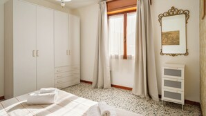 Een slaapkamer met een bed, een kast, een radiator en een raam met gordijnen.