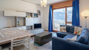 Een moderne woonkamer met een bank, een eettafel, een televisie en uitzicht op bergen door grote ramen.