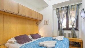 Un dormitorio con cama, armario de madera, ventana con cortinas y radiador.
