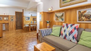 Una sala de estar acogedora con piso de madera, un sofá con cojines coloridos, una mesa de comedor con sillas y obras de arte enmarcadas en las paredes.